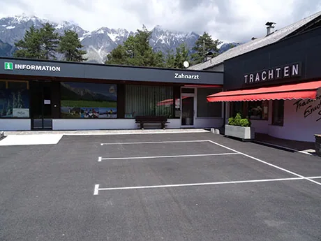 Praxisgebäude mit Schild Zahnarzt, freier Parkplatz davor, dahinter die Mieminger Kette